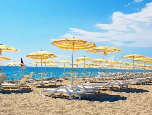 Spiaggia soleggiata con ombrelloni gialli e mare azzurro, atmosfera estiva e rilassante.