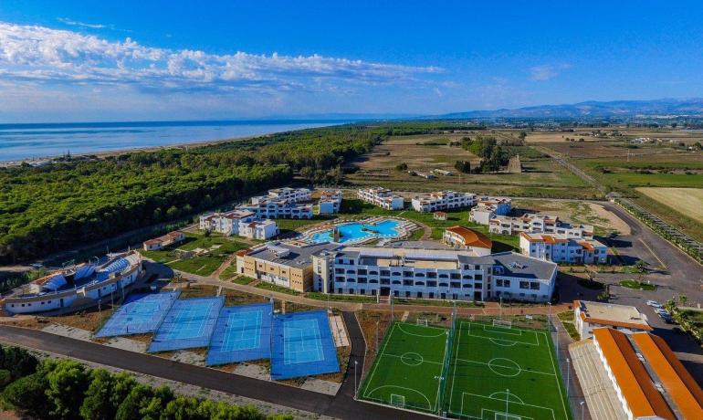 Vista aerea di un resort con piscine e campi sportivi vicino al mare.