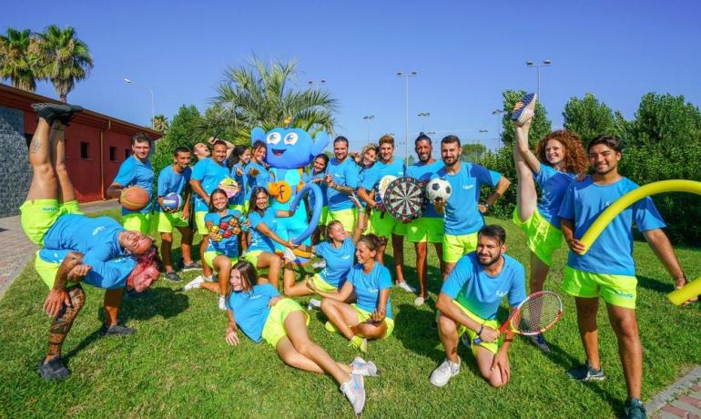 Gruppo allegro con magliette blu e pantaloncini gialli, circondato da giochi all'aperto.