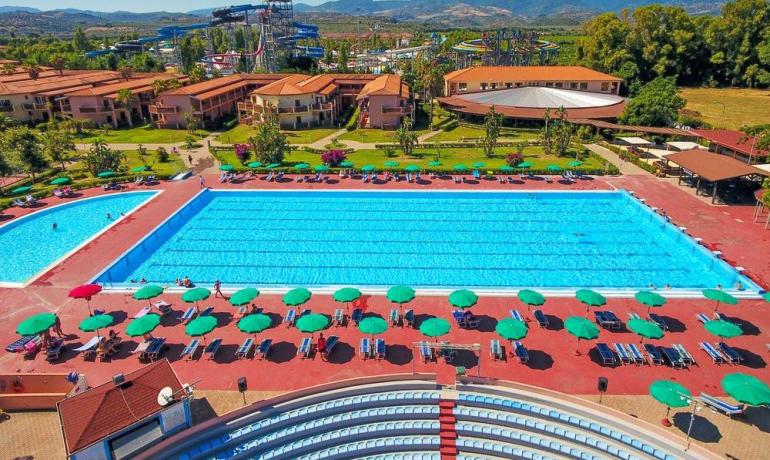 Piscina estiva, ombrelloni colorati, montagne sullo sfondo, atmosfera rilassante e divertente.