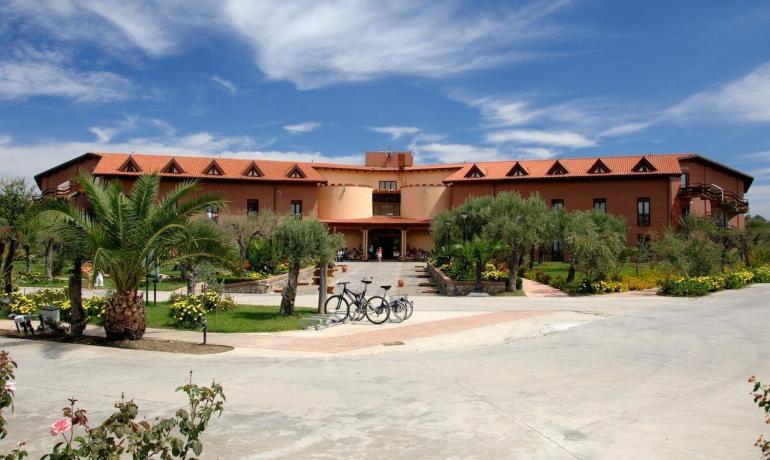Edificio rustico con giardino fiorito, cielo azzurro e biciclette parcheggiate.