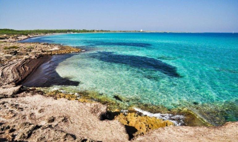 Spiaggia rocciosa, mare turchese e cielo limpido evocano pace e serenità.