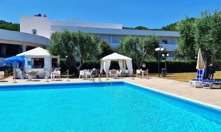 Piscina luminosa, cielo azzurro, relax sotto gazebo bianchi tra ulivi.