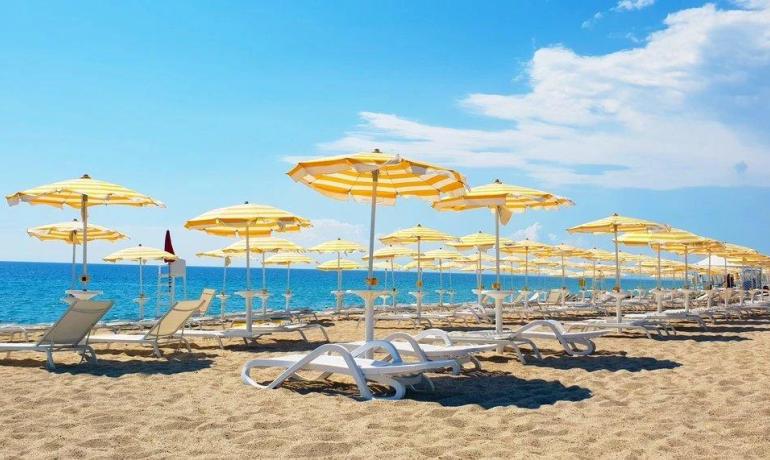 Spiaggia soleggiata con ombrelloni gialli e mare azzurro, atmosfera estiva e rilassante.