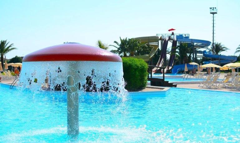 Piscina con fontana a fungo, scivoli e atmosfera estiva vivace.