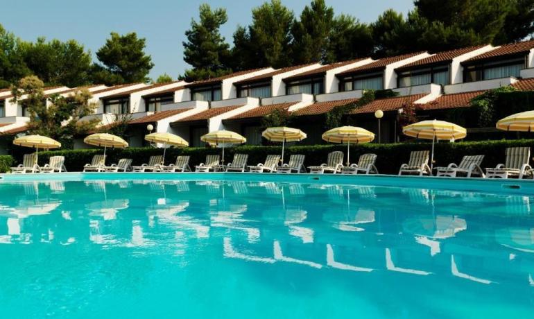 Piscina azzurra, ombrelloni gialli, relax e natura circostante.