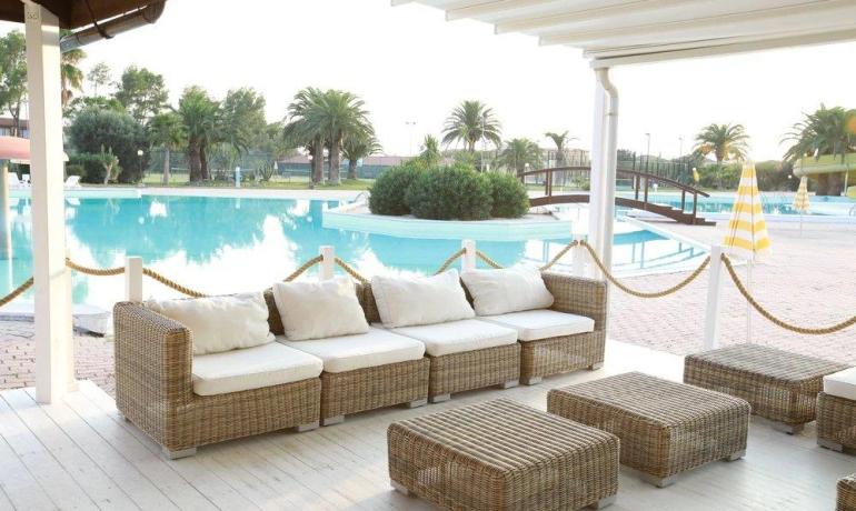 Piscina rilassante con divani in vimini, palme e atmosfera estiva.