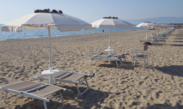 Spiaggia serena con ombrelloni bianchi e mare calmo all'orizzonte.