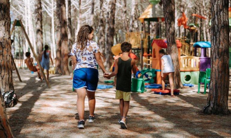 Bambini giocano felici in un parco giochi tra alberi alti e colorati.