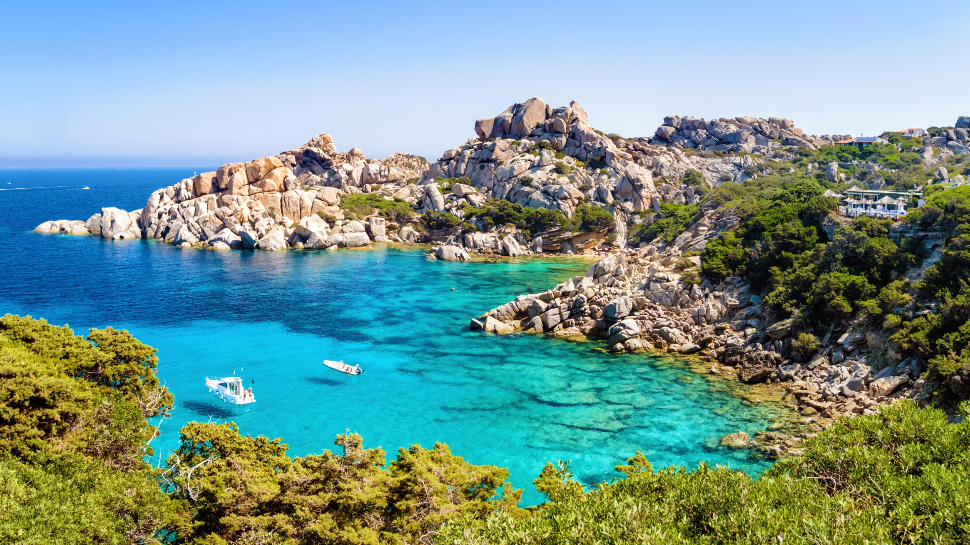 Spiaggia con acque turchesi, rocce imponenti e vegetazione mediterranea.