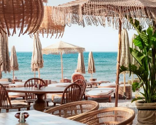 Spiaggia con ombrelloni di paglia, sedie in legno e vista sul mare azzurro.