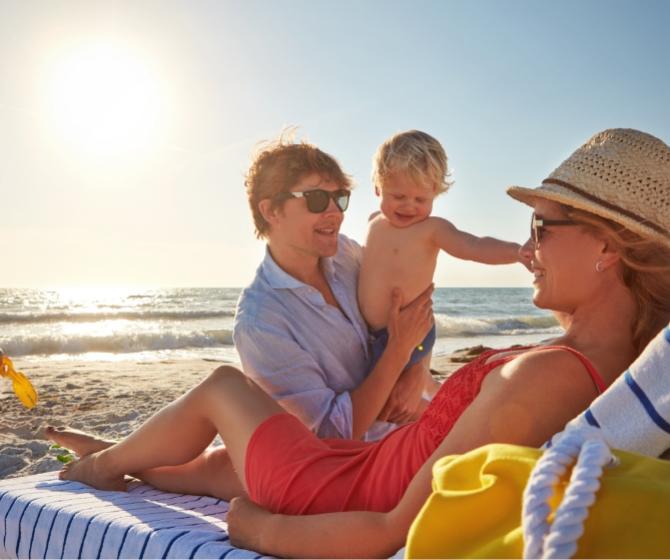 Famiglia felice in spiaggia, godendo il sole e il mare insieme.